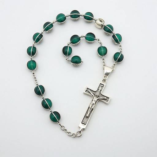 Photograph of a silver crucifix rosary with dark green oval beads, arranged in a circular pattern on a white background.