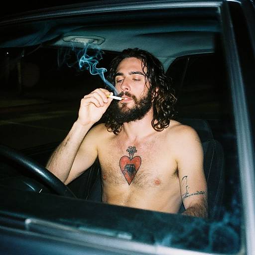 Photograph of shirtless bearded man with long dark hair, smoking cigarette, heart tattoo on chest, 