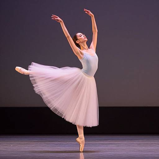 Photograph of a graceful ballerina in a white tutu and leotard, balancing on pointe, arms raised, dancing on a dark