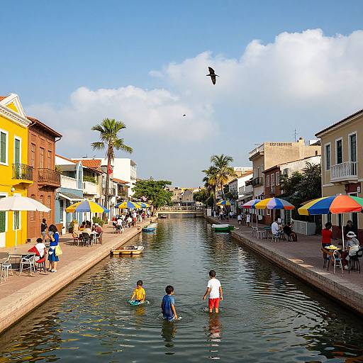 Vibrant photograph of a sunny canal in a tropical town, with children wading, colorful umbrellas, people dining, and buildings lining the water