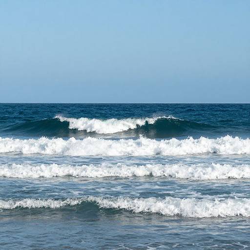 Photograph of a clear blue ocean with white foam waves breaking against the dark blue water under a bright, cloudless sky.