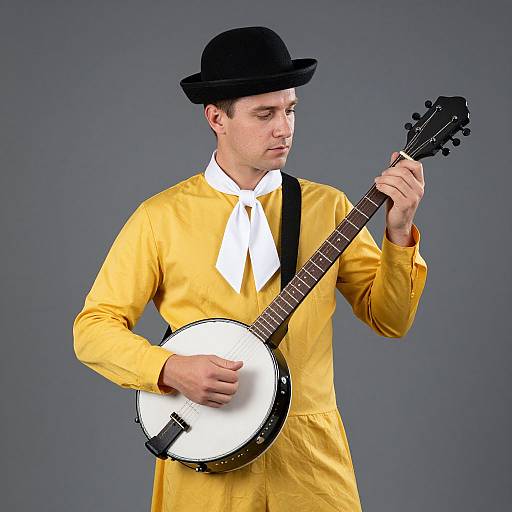 Photograph of a young man in a yellow shirt, white bow tie, black hat, playing a banjo against a gray background.