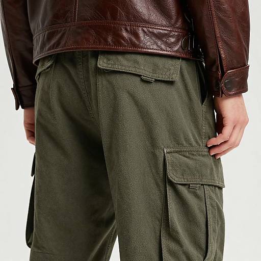 Photograph of a person's lower torso, wearing dark green cargo pants and a brown leather jacket, hand resting on right pocket.