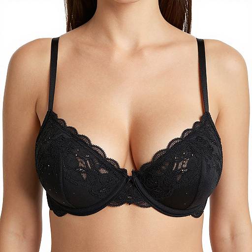 Photograph of a woman's upper chest, wearing a black lace bra with sheer, floral-patterned fabric and thin straps, against a plain white background