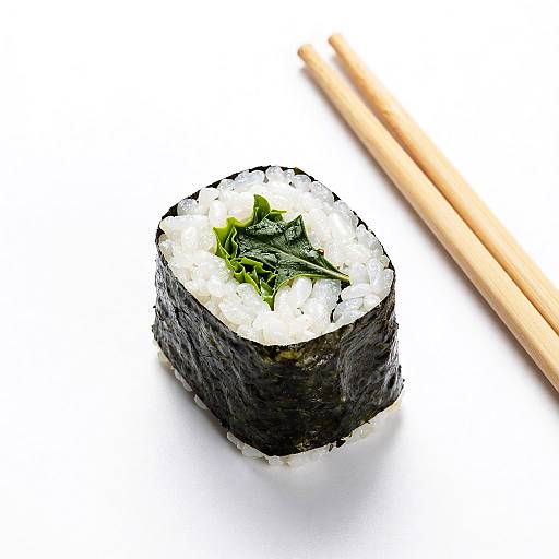 Photograph of a sushi roll with white rice, black seaweed, green leaf garnish, and wooden chopsticks on a white background.