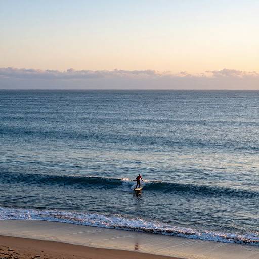 Photograph of a lone surfer riding a small wave near a sandy beach at sunset, with a gradient sky from orange to blue.