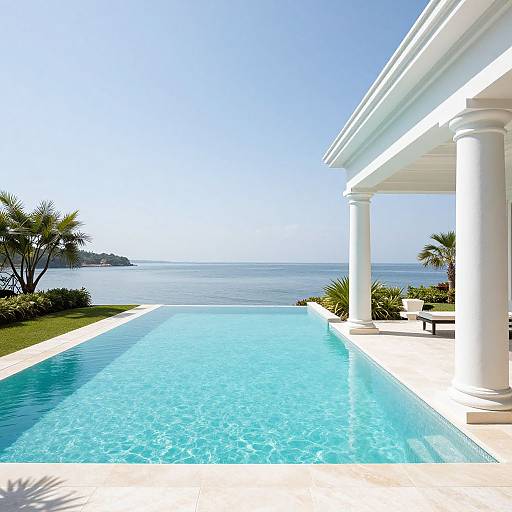 Photograph of a luxurious poolside view: clear turquoise pool, white-columned patio, palm trees, and serene ocean horizon under bright blue sky.