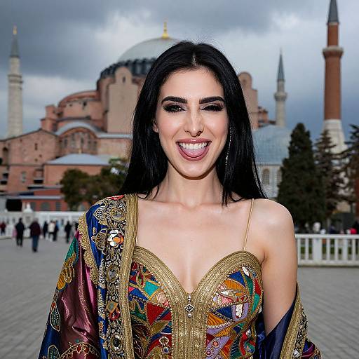 Photograph of a smiling woman with long black hair, wearing an ornate, colorful, strapless dress, in front of Istanbul's Blue Mosque.