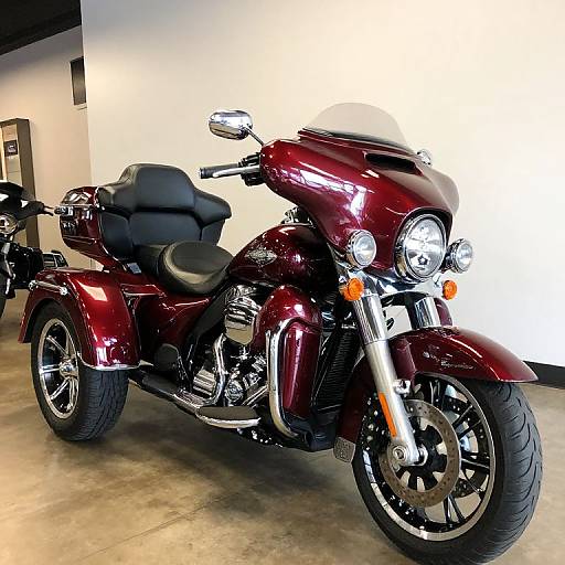 Photograph of a shiny maroon touring motorcycle with black leather seat, chrome accents, dual headlights, and large front tire, parked in a brightly lit