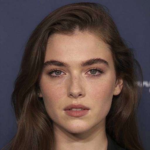 Photograph of a young woman with fair skin, blue eyes, and dark brown hair, wearing subtle makeup, against a dark blue background.