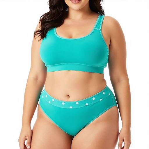 Photograph of a curvy woman with light brown skin wearing a turquoise sports bra and high-waisted panties with white polka dots, against a