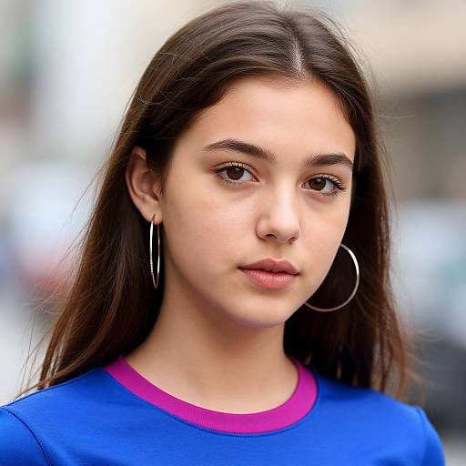 Photograph of a young woman with long brown hair, fair skin, and brown eyes, wearing a blue shirt with a pink collar, and large silver
