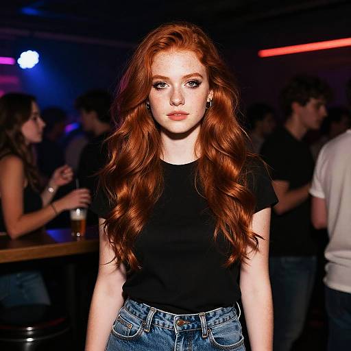 Photograph of a red-haired woman with long wavy hair, wearing a black top and blue jeans, in a dimly lit nightclub with blurred background
