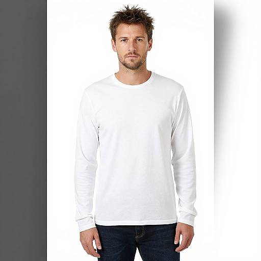 Photograph of a Caucasian man with spiked brown hair, beard, wearing a plain white long-sleeve shirt and dark blue jeans, standing against a