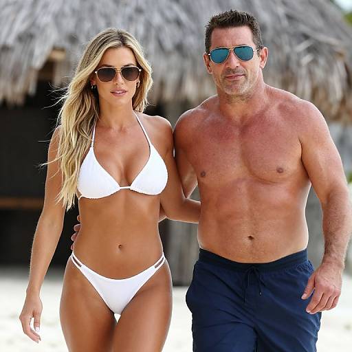 Photograph of a fit, blonde woman in a white bikini and sunglasses, walking with a muscular, tanned man in blue swim trunks and sunglasses
