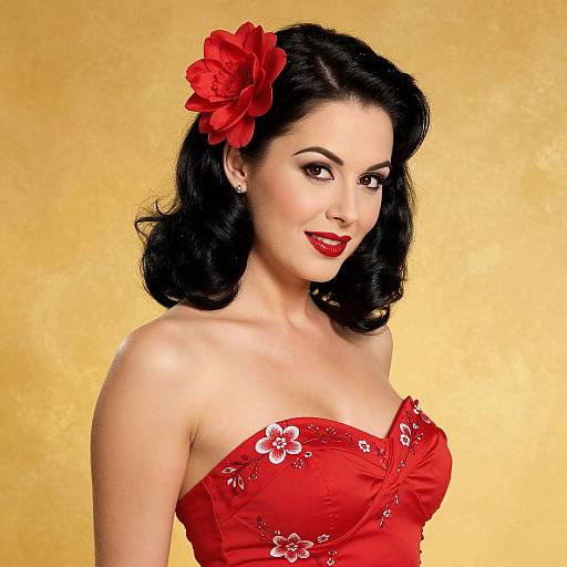 Photograph of a fair-skinned woman with black, wavy hair, wearing a red strapless dress with floral embroidery, and a large red flower