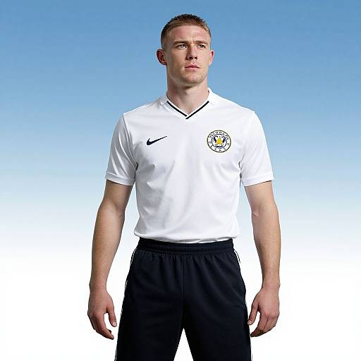 Photograph of a Caucasian male soccer player with short brown hair, wearing a white Germany national team jersey and black shorts, standing against a blue gradient background