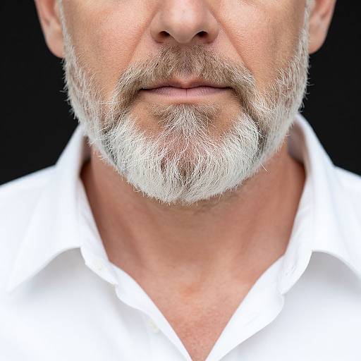 Close-up photograph of a white-bearded man's face and upper chest, wearing a white collared shirt, against a black background.