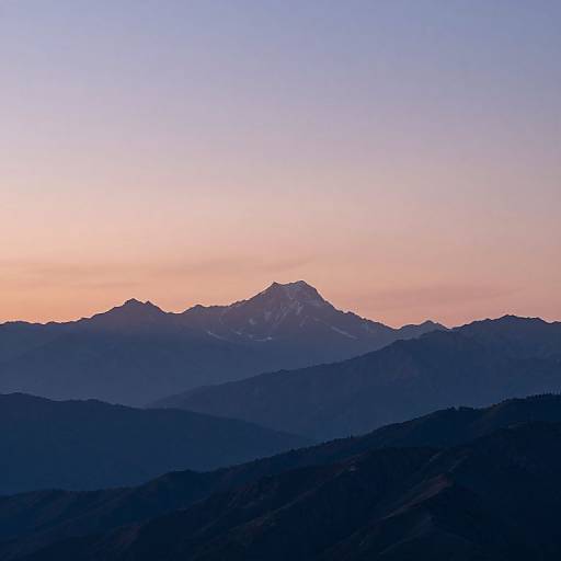 Photograph of a mountain range at sunset, with a gradient sky from pink to blue, and dark blue silhouetted foreground hills.