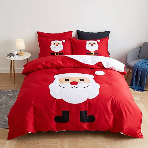 Photograph of a bed with red Santa-themed bedding, featuring white cartoon Santa faces on pillows and duvet, next to a white nightstand and gray