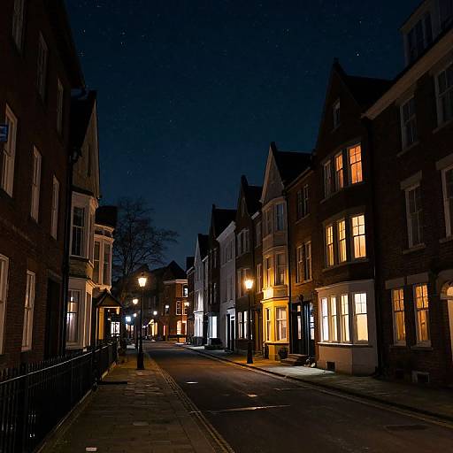 Photograph of a quiet, narrow, illuminated European street at night, with starry sky, lit windows, and classic brick buildings.
