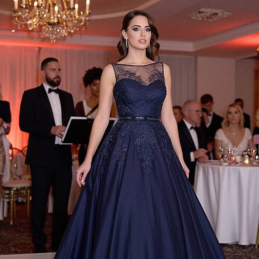 Photograph of a beautiful woman with long brown hair in a black lace and tulle gown, standing in an elegant ballroom with chandeliers,