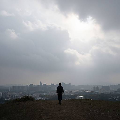 Silhouetted person walking towards bright, overcast sky with city skyline in the distance; photograph capturing serene, urban morning scene.