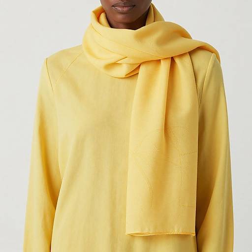 Photograph of a person with dark skin wearing a bright yellow oversized scarf and matching yellow long-sleeve shirt.