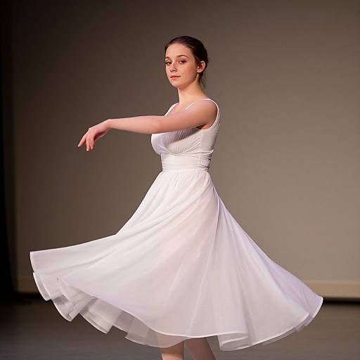 Photograph of a fair-skinned woman with dark hair in a white, sleeveless, knee-length dress, gracefully posing against a plain gray background,