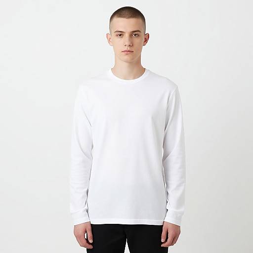 Photograph of a young, fair-skinned man with a shaved head, wearing a plain white long-sleeve shirt and black pants, standing against