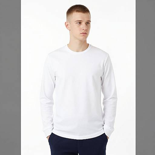 Photograph of a young man with short brown hair, fair skin, wearing a plain white long-sleeve shirt and dark pants, standing against a