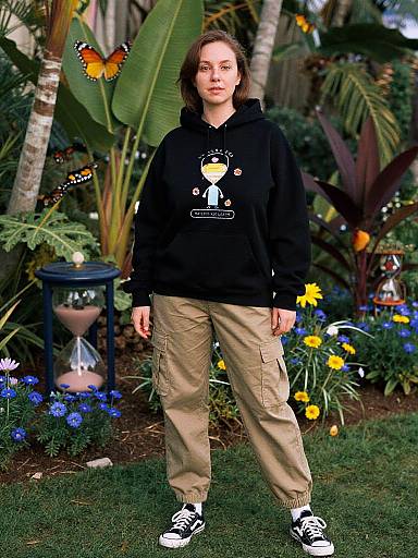 Photograph of a woman with shoulder-length brown hair, wearing a black hoodie, beige cargo pants, and black-and-white sneakers, standing in a vibrant
