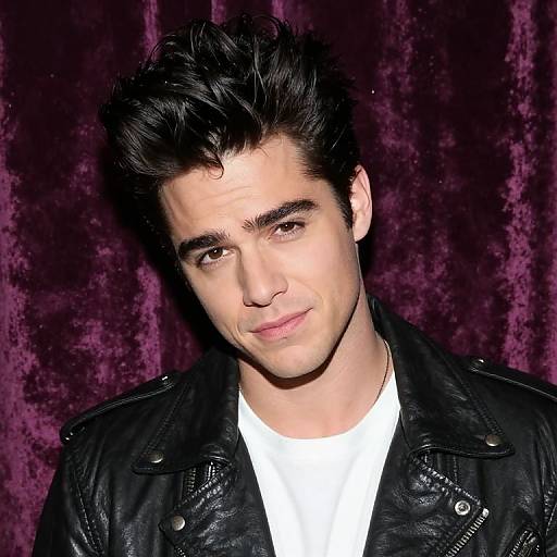 Photograph of a young man with dark, tousled hair, light skin, and brown eyes, wearing a black leather jacket over a white shirt,
