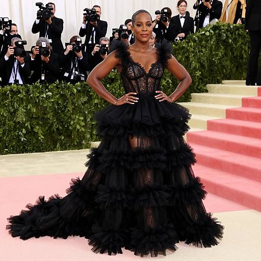 Photograph of Beyoncé in a black, layered, ruffled gown with lace bodice, standing confidently on red carpet, surrounded by photographers.