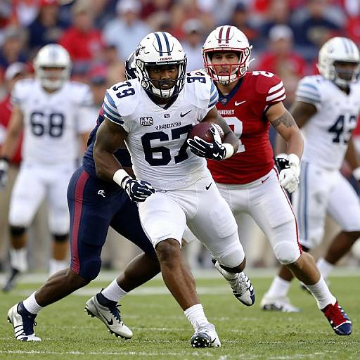 Photograph of a football game: Black running back in white uniform with number 6, pursued by white and red uniformed player. Blurred crowd