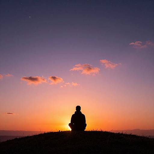 Silhouetted person sitting on a hill, watching a vibrant sunset with a gradient sky of purple, orange, and pink.