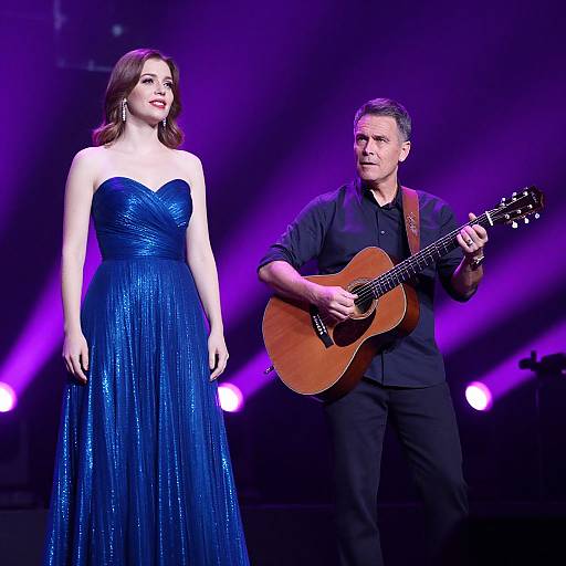 Photograph of a woman in a sparkling blue strapless gown and a man in black playing an acoustic guitar on a purple-lit stage.