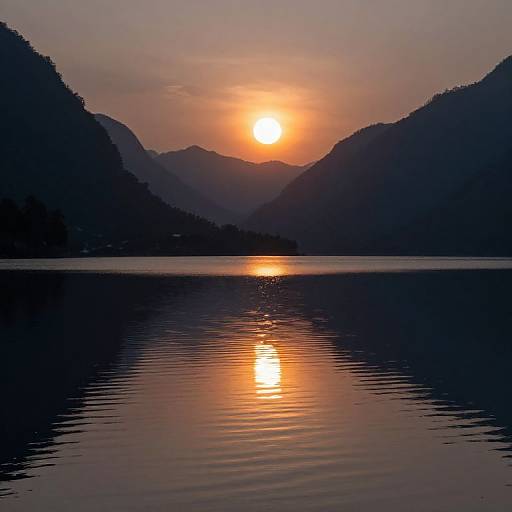 Photograph of a serene sunset over a calm lake, with silhouetted mountains on either side, reflecting the orange sun on the water.