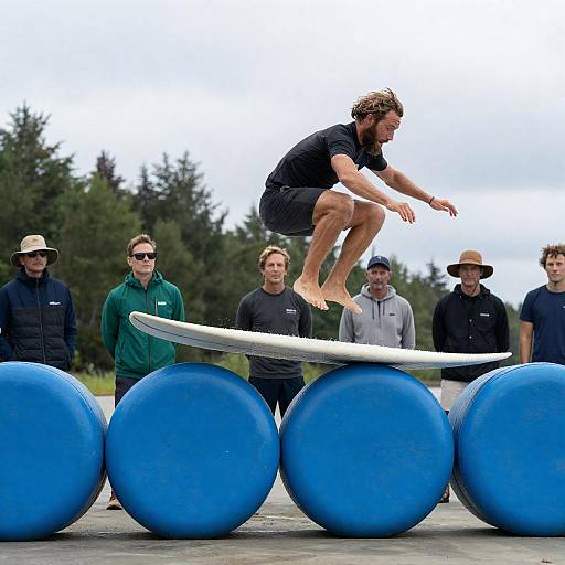 Man Balancing Mid-Air on Surfboard Over Blue Barrels