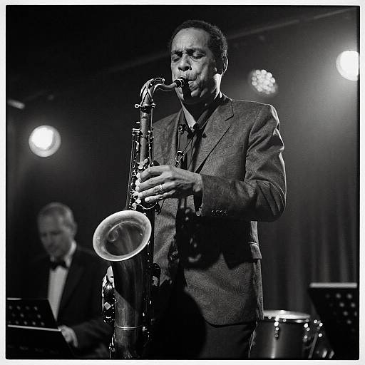 Black-and-white photograph of a middle-aged man in a suit playing a saxophone on stage, with another musician in the background.