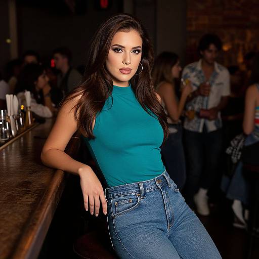 Photograph of a brunette woman with long hair, wearing a teal sleeveless top and blue jeans, leaning against a bar in a dimly lit,