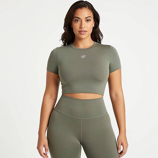 Photograph of a confident woman with olive skin, long black hair, wearing a green cropped athletic top and matching high-waisted leggings, standing against