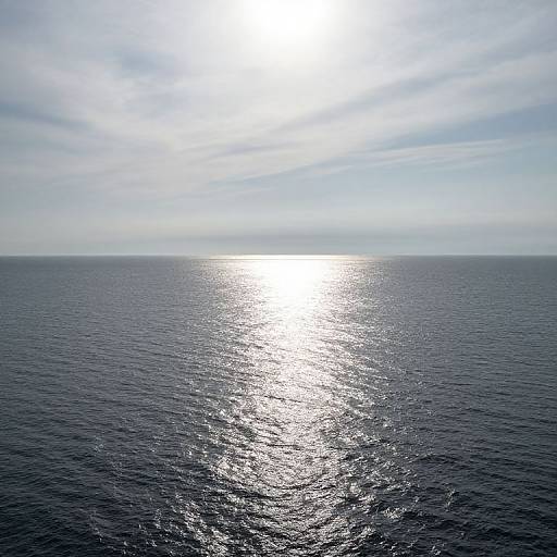 Photograph of a bright, sunlit ocean horizon with a dazzling, silver sun reflection on dark blue water, under a lightly cloudy sky.