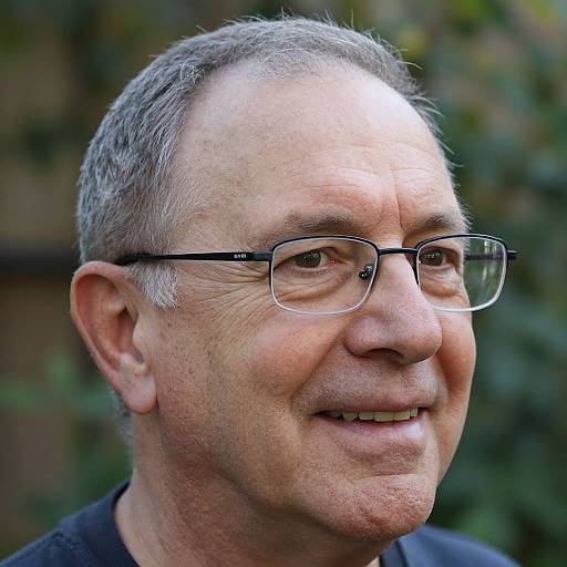 Photograph of middle-aged man with short gray hair, glasses, light skin, smiling slightly, wearing black shirt, against blurred green background.