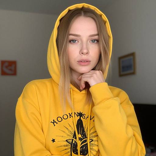 Photograph of a fair-skinned, blue-eyed young woman with straight, shoulder-length brown hair, wearing a yellow hooded sweatshirt with a black