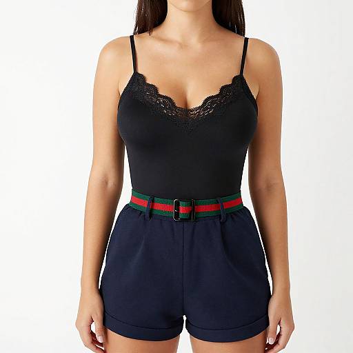 Photograph of a woman with light skin wearing a black lace-trimmed camisole and high-waisted black shorts with a red and green
