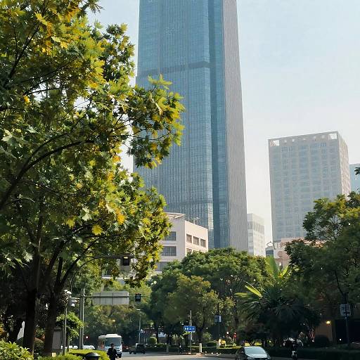 Photograph of a cityscape with a towering glass skyscraper, surrounded by lush green trees, and smaller buildings in the background.