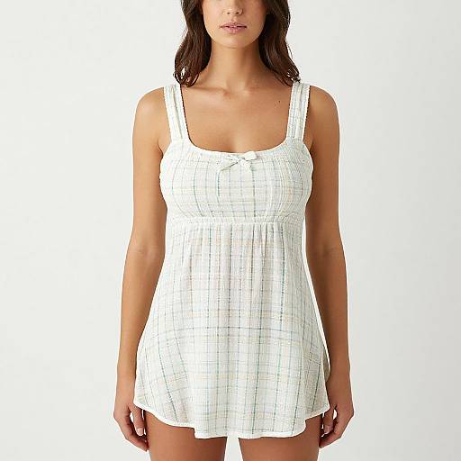 Photograph of a woman with medium brown hair, wearing a white, checkered, sleeveless, loose-knit dress, standing against a plain white