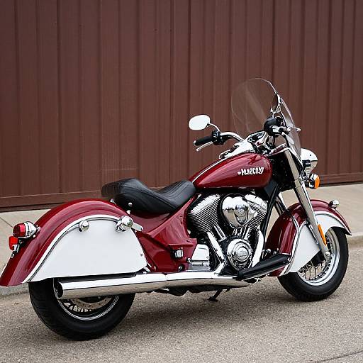 Photograph of a shiny red and white Harley-Davidson motorcycle with chrome details, black leather seat, and a clear windshield, parked against a brown