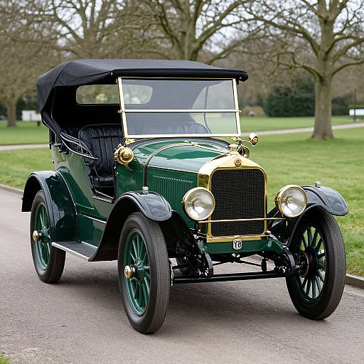 Photograph of a vintage green classic car with black convertible top, gold accents, and large headlights, parked on a paved path in a park with leaf